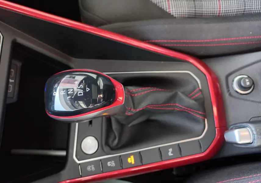 Gros plan sur le levier de vitesses automatique rouge et noir de la Volkswagen Polo GTI 2024, avec surpiqûres rouges visibles.