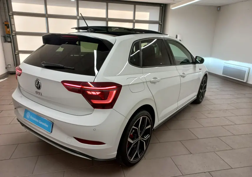 Volkswagen Polo GTI blanc pur avec toit noir, vue 3/4 arrière droit, feux allumés et jantes sport noires.