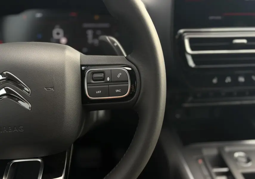 Gros plan sur le volant noir du Citroën C5 Aircross 2025 avec commandes intégrées et tableau de bord flou en arrière-plan.