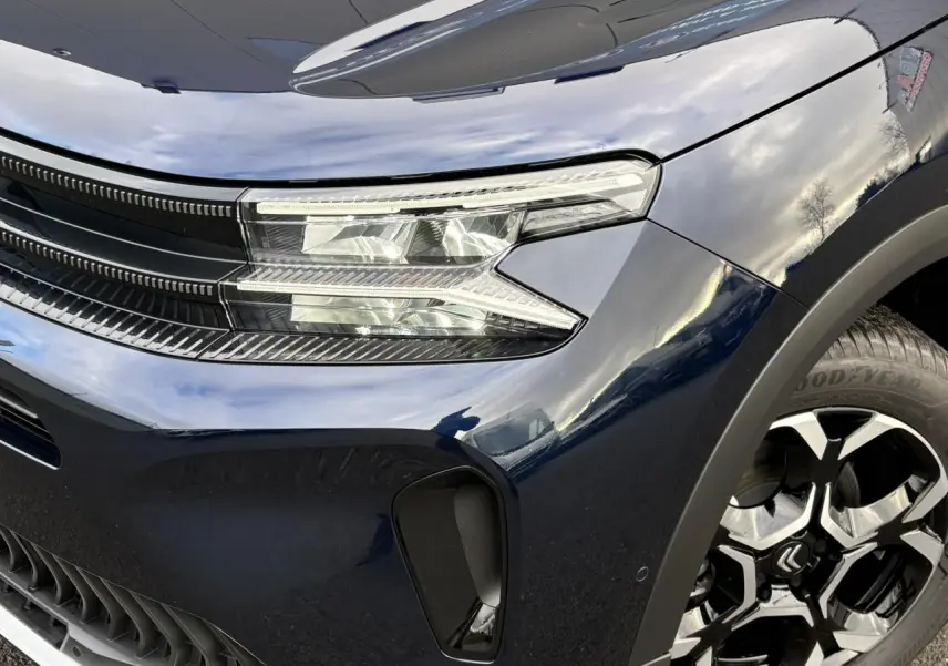 Gros plan sur l'avant droit bleu Eclipse du Citroën C5 Aircross 2025, mettant en valeur le phare LED et la jante alliage bi-ton.