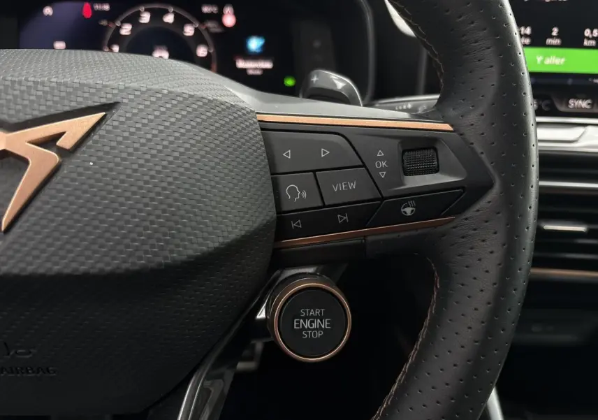Gros plan sur le volant cuir perforé et le bouton Start Engine Stop du CUPRA LEON ST 2025, détails en cuivre et commandes intégrées.
