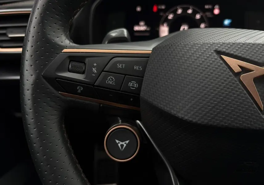Gros plan sur le volant cuir perforé noir du CUPRA LEON ST 2025 avec logo cuivre et commandes intégrées à gauche.