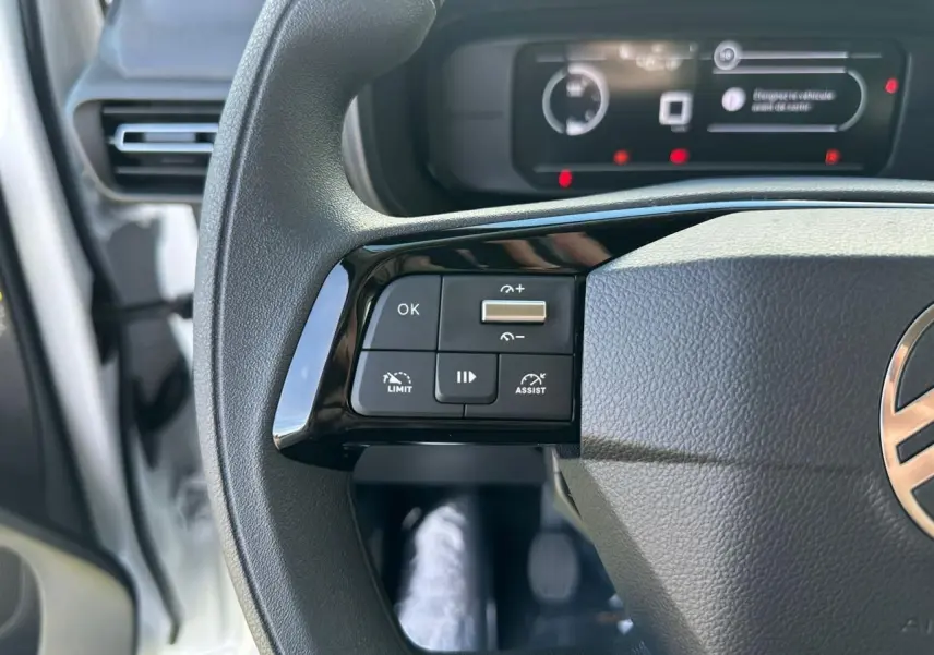 Gros plan sur les commandes au volant côté gauche du Citroën Berlingo blanc, avec tableau de bord numérique en arrière-plan.