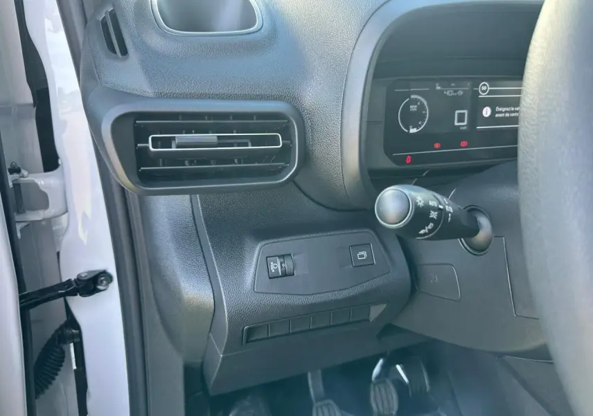 Vue rapprochée côté gauche du tableau de bord noir avec commandes d'éclairage et pédales du Citroën Berlingo blanc Icy.