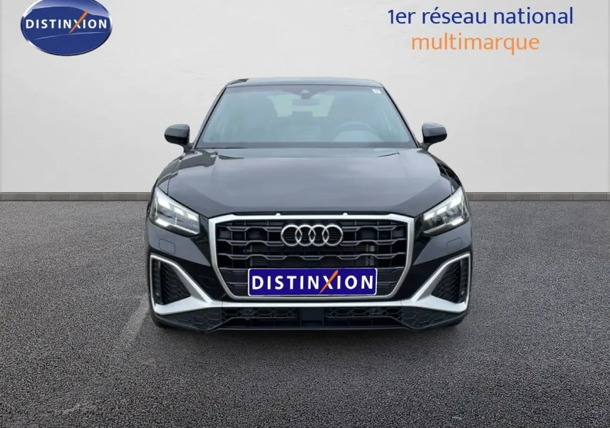 Vue frontale d'un Audi Q2 noir mito metal avec calandre hexagonale et phares LED allumés sur parking.