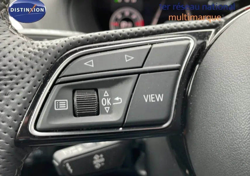 Gros plan sur les commandes gauche du volant perforé d’un Audi Q2 noir, avec boutons directionnels et fonction View.