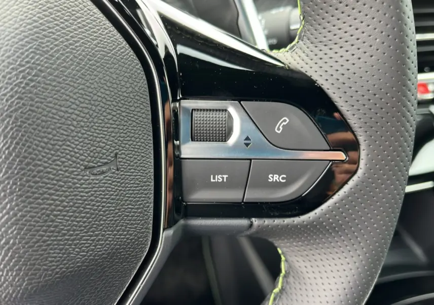 Gros plan sur les commandes gauche du volant cuir perforé de la Peugeot 2008 Hybrid 145 GT Vision 2025.