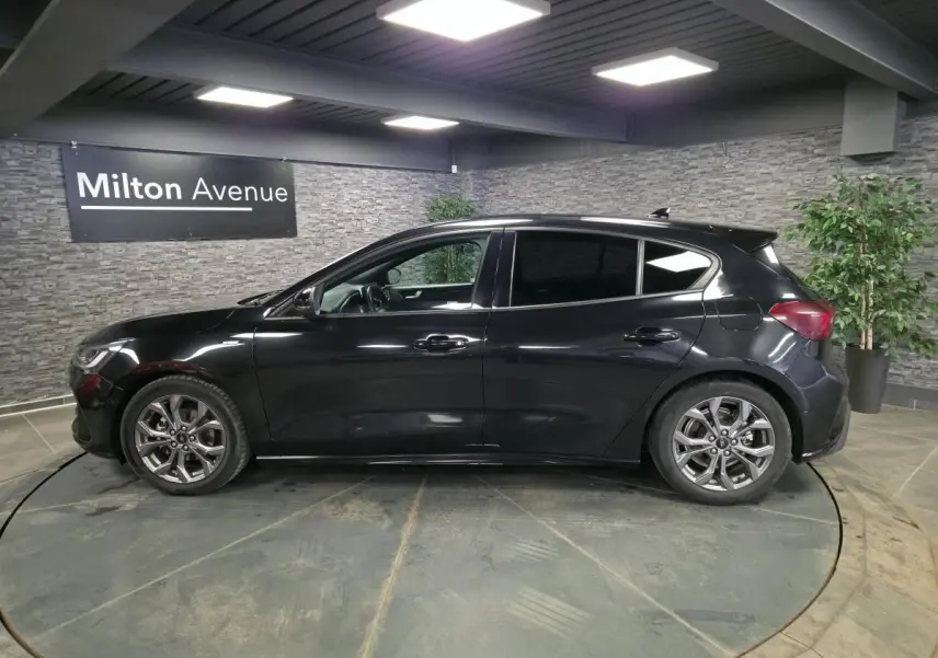 Vue de profil côté gauche d'une Ford Focus noire 2024 ST Line avec jantes alliage 17 pouces dans un showroom.