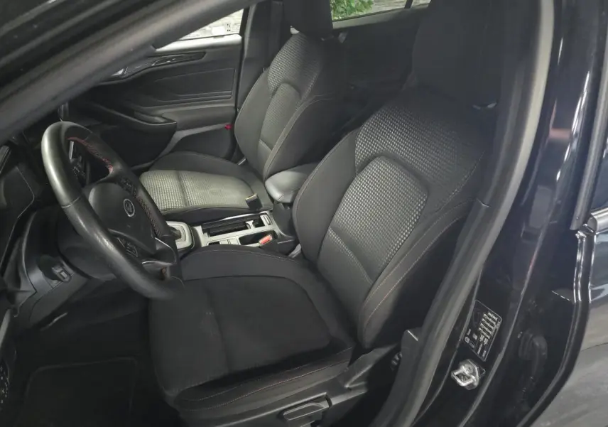 Vue intérieure côté conducteur de la Ford Focus noire 2024, sièges tissu ST-Line avec surpiqûres rouges et volant sport.