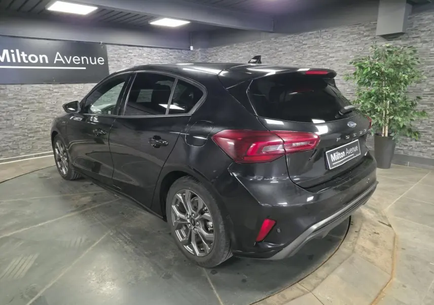 Ford Focus noire 2024 vue 3/4 arrière droit, jantes alliage 17'' et feux arrière LED dans un showroom.