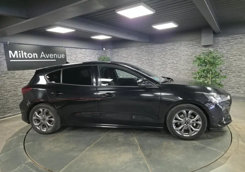 Vue de profil côté gauche d'une Ford Focus noire 2024 ST Line avec jantes alliage 17 pouces en intérieur showroom.