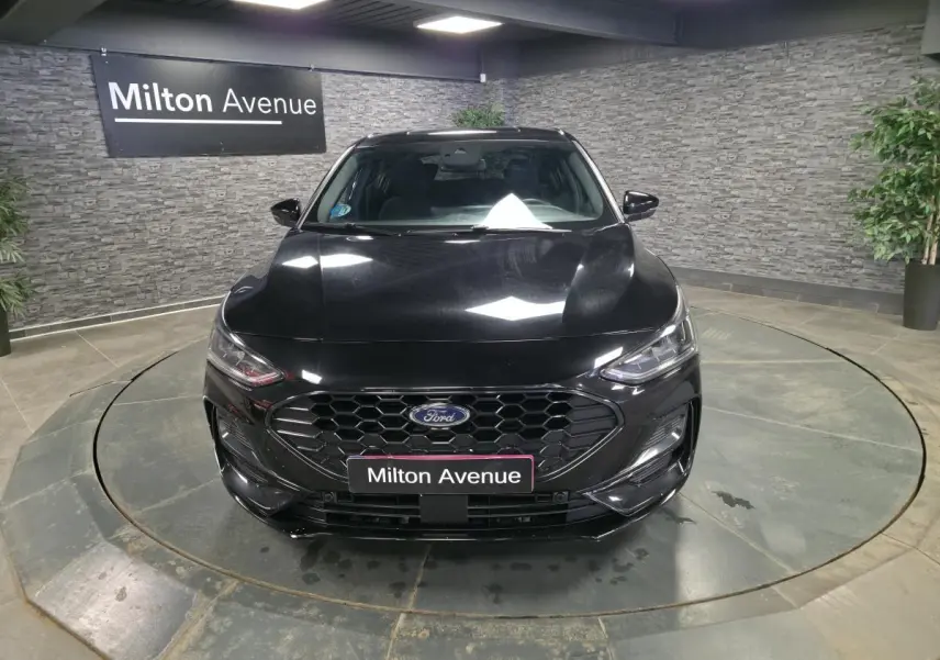 Vue avant d'une Ford Focus noire 2024 avec calandre noire hexagonale et badge ST-Line visible en intérieur showroom.
