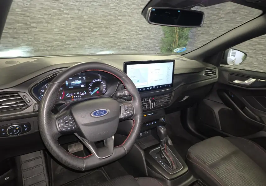 Vue intérieure avant droite de la Ford Focus 2024, volant ST Line noir avec surpiqûres rouges et écran tactile central.