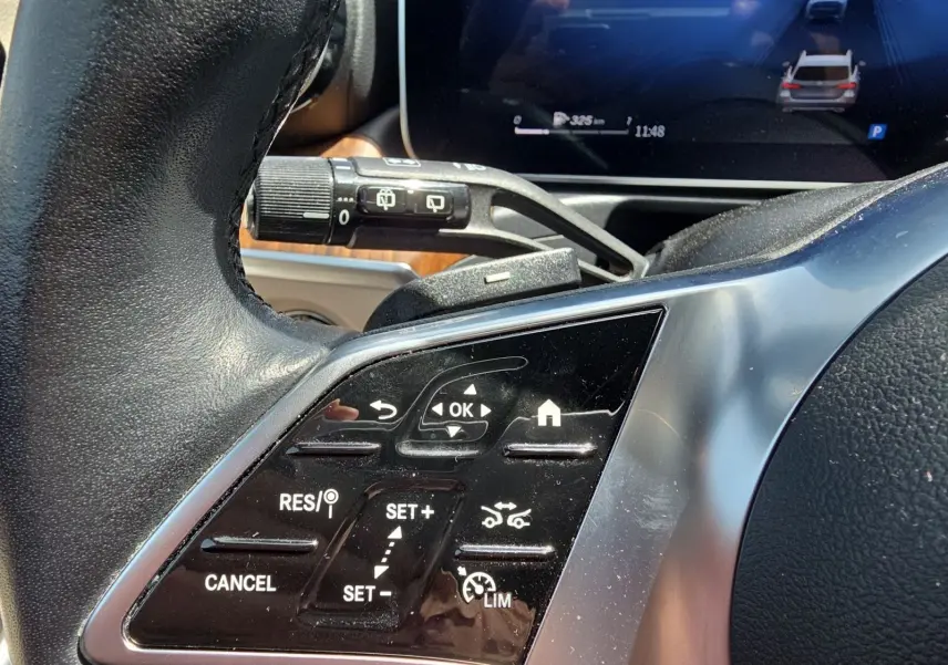 Gros plan sur les commandes au volant noir d’une Mercedes Classe C Break gris foncé, avec régulateur de vitesse adaptatif.