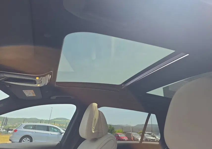 Vue intérieure du toit ouvrant panoramique et des sièges avant en cuir clair d’un break Mercedes Classe C gris foncé.