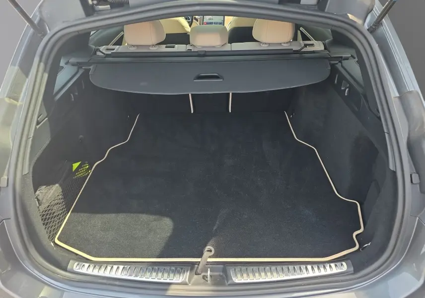 Vue arrière du coffre ouvert d’un Mercedes Classe C Break gris foncé, avec tapis noir et cache-bagages déployé.