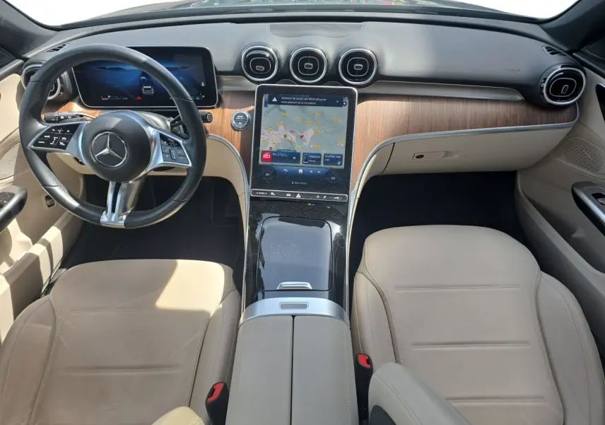 Vue intérieure avant du Mercedes Classe C Break 220 D 4MATIC avec sellerie cuir beige et tableau de bord bois et écran tactile central.