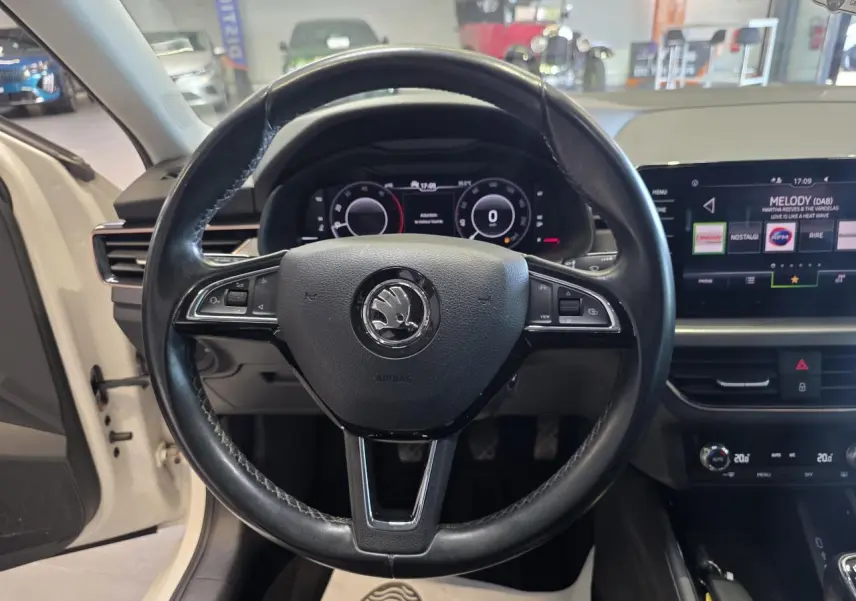 Vue frontale centrée sur le volant cuir noir de la Skoda Scala blanche, avec tableau de bord digital et écran tactile visible.