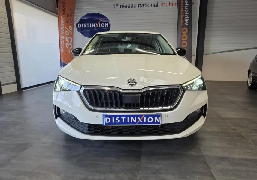 Vue frontale d'une Skoda Scala blanche avec calandre noire et phares LED allumés en intérieur showroom.