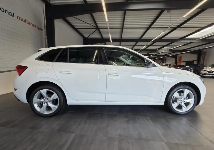 Vue latérale droite d'une Skoda Scala blanche 2020 avec jantes alliage argent et vitres teintées en intérieur showroom.