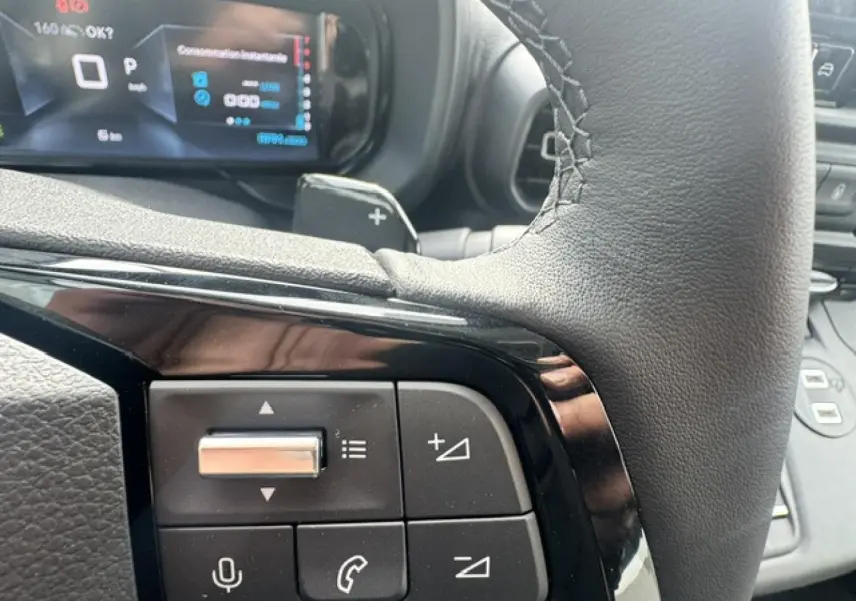 Gros plan sur les commandes au volant cuir noir du Citroën Berlingo 2026, affichage numérique en arrière-plan.