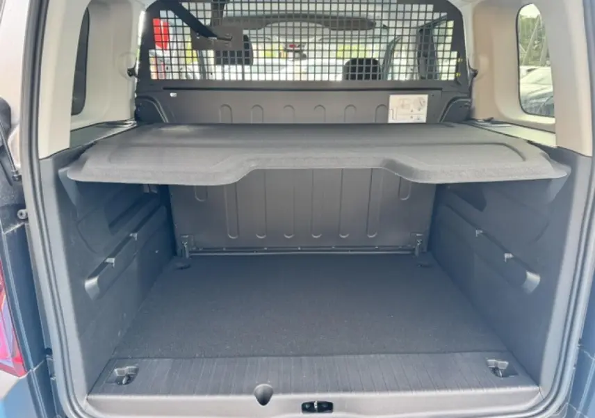 Coffre ouvert vu de l'arrière d'un Citroën Berlingo gris acier avec tablette de séparation et grille de protection.