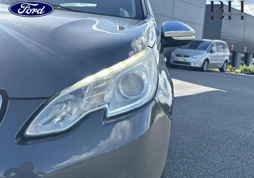 Gros plan sur le phare avant droit d'un Peugeot 2008 Spirit Grey, avec rétroviseur chromé et reflet du ciel.