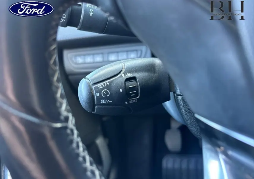Gros plan sur la commande de régulateur de vitesse noire, vue depuis le volant d’un véhicule Ford.