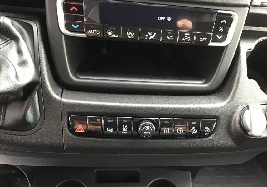 Vue rapprochée de la console centrale du Peugeot Boxer Fourgon blanc, montrant les commandes climatisation et boutons multifonctions.