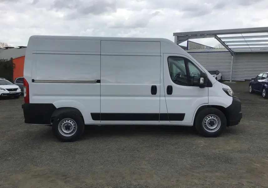 Vue latérale droite d'un utilitaire Peugeot Boxer Fourgon blanc, avec porte coulissante et protections noires sur les bas de caisse.