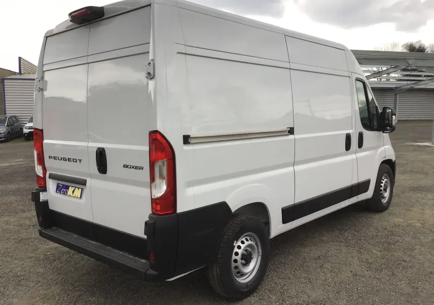 Vue 3/4 arrière droite d'un Peugeot Boxer blanc 2025 avec hayon arrière fermé et protections noires sur les bas de caisse.