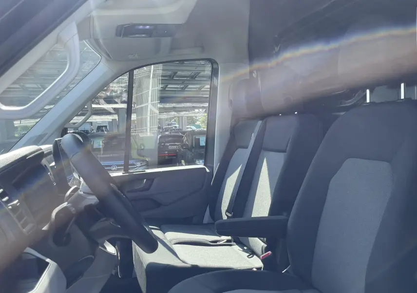 Vue intérieure côté conducteur du Volkswagen Crafter Van 2025 avec sièges tissu gris et cloison vitrée arrière.