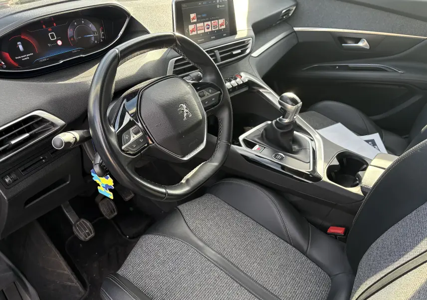 Vue intérieure avant droite du Peugeot 3008 2019, volant compact, sellerie mixte cuir-tissu grise et console centrale avec boîte manuelle.