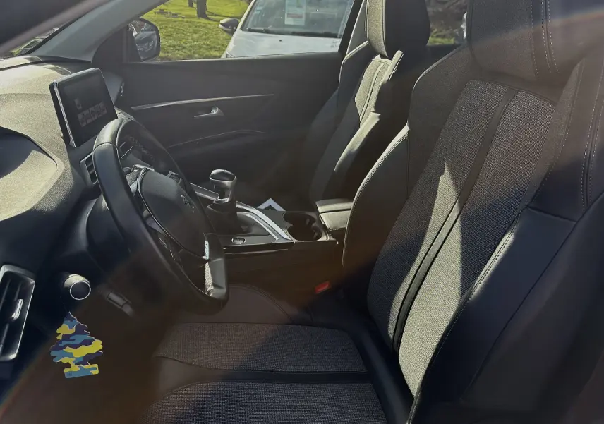 Vue intérieure côté conducteur du Peugeot 3008 II 2019, sièges en tissu et cuir noir avec console centrale et volant visible.