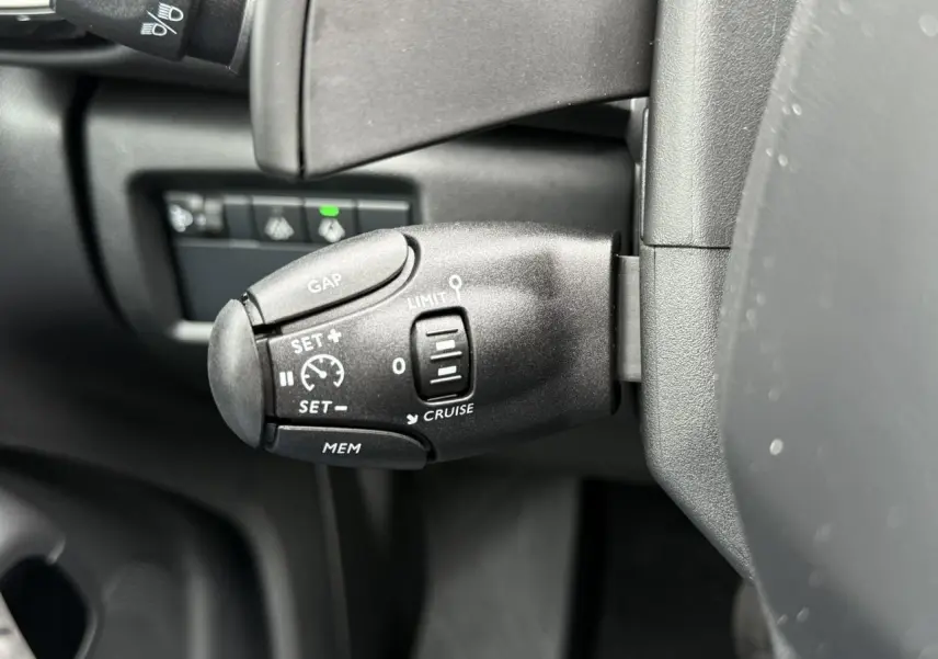 Gros plan sur la commande de régulateur de vitesse à gauche du volant dans l'habitacle noir du Citroën C5 Aircross 2025.
