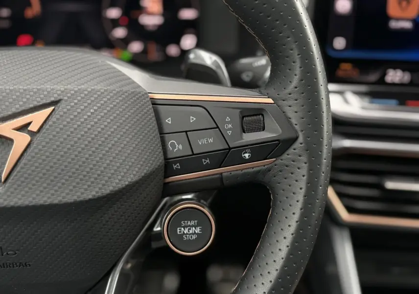 Gros plan sur le volant perforé noir avec logo CUPRA cuivré et bouton start/stop, intérieur moderne et détails cuivrés.