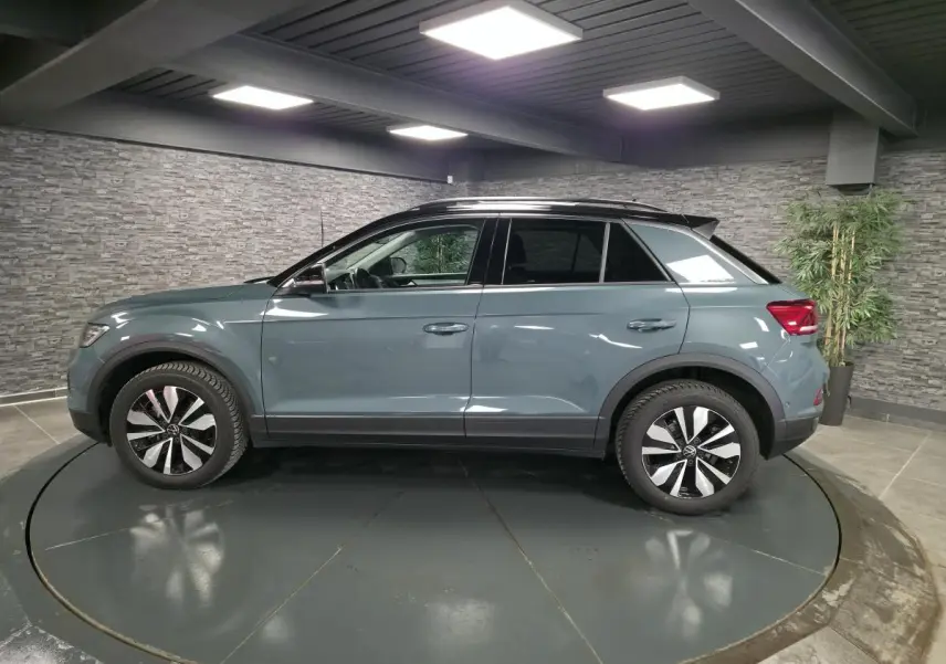 Vue de profil côté gauche d'un Volkswagen T-Roc bleu métallisé avec toit noir dans un showroom.