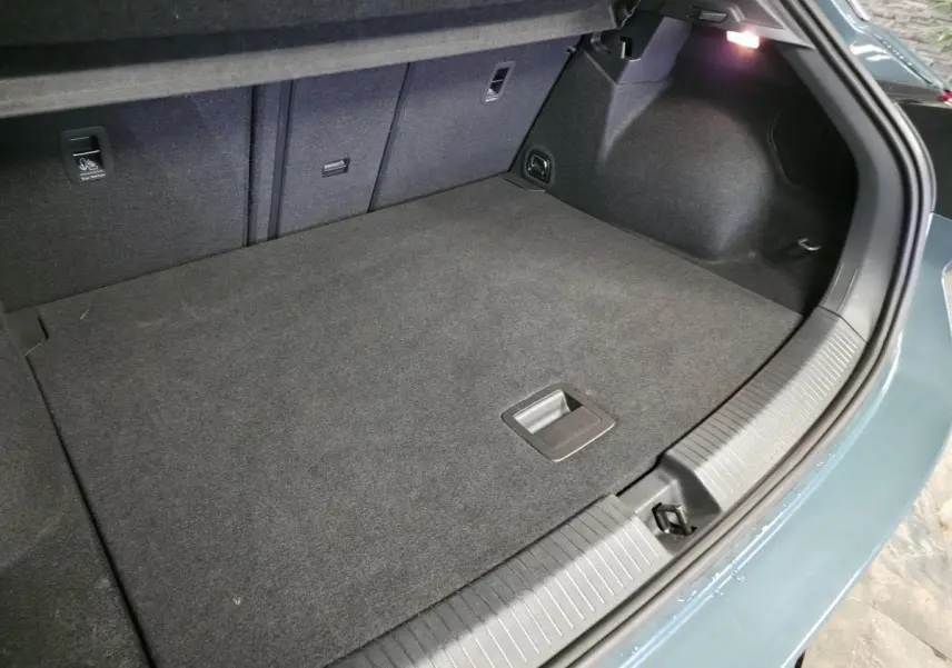 Vue intérieure du coffre spacieux du Volkswagen T-Roc bleu, avec tapis gris foncé et éclairage latéral.