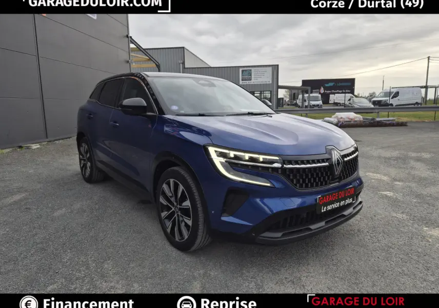 Renault Austral bleu 3/4 avant droit avec calandre noire et phares LED allumés sur parking extérieur.