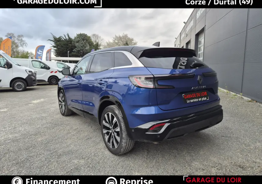 Vue 3/4 arrière droite d'un Renault Austral bleu avec toit noir et jantes alliage, stationné devant un bâtiment gris.