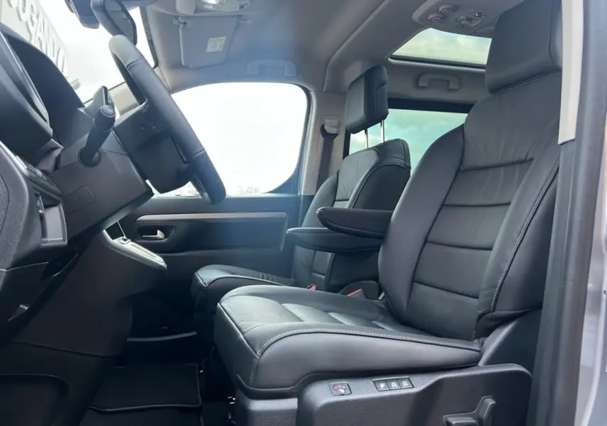 Vue intérieure côté conducteur du Citroën Spacetourer gris acier, sièges avant cuir noir avec accoudoir et toit panoramique.