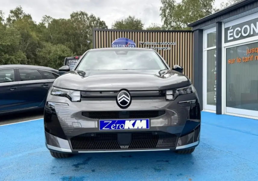 Vue frontale d'un Citroën C5 Aircross gris Platinium avec logo distinctif et plaque "Zéro KM" sur un sol bleu.