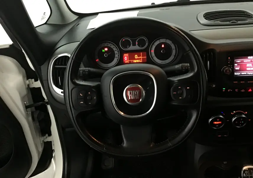 Vue intérieure centrée sur le volant noir de la Fiat 500L blanche, avec tableau de bord et commandes visibles.