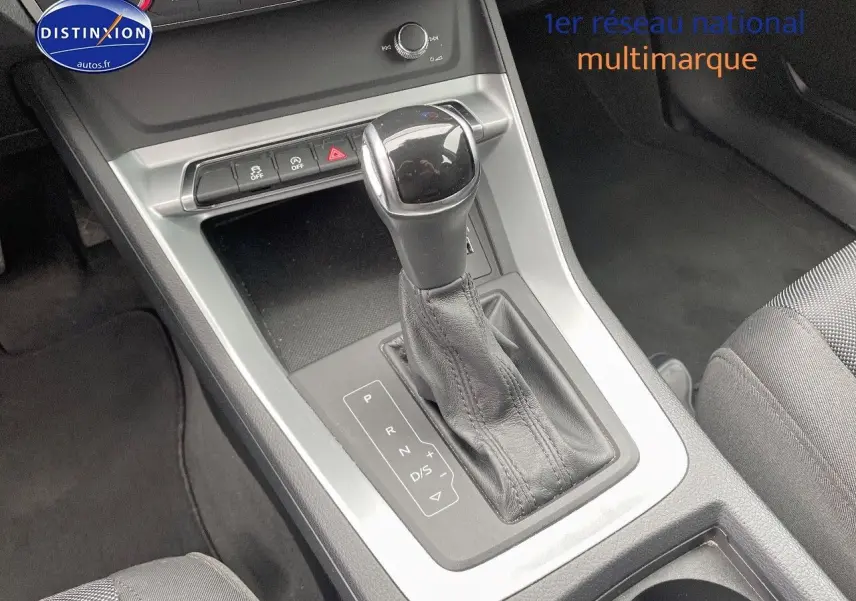 Le levier de vitesses automatique de l'Audi Q3 35 TFSI 150CH en gros plan, avec console grise et sellerie tissu noire.