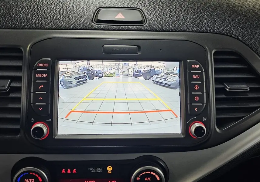 Écran central de la KIA PICANTO blanche 2016 montrant la caméra de recul avec les lignes de guidage colorées.