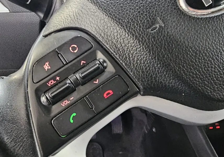 Gros plan sur les commandes audio et téléphone au volant en cuir noir d'une KIA Picanto blanche de 2016.
