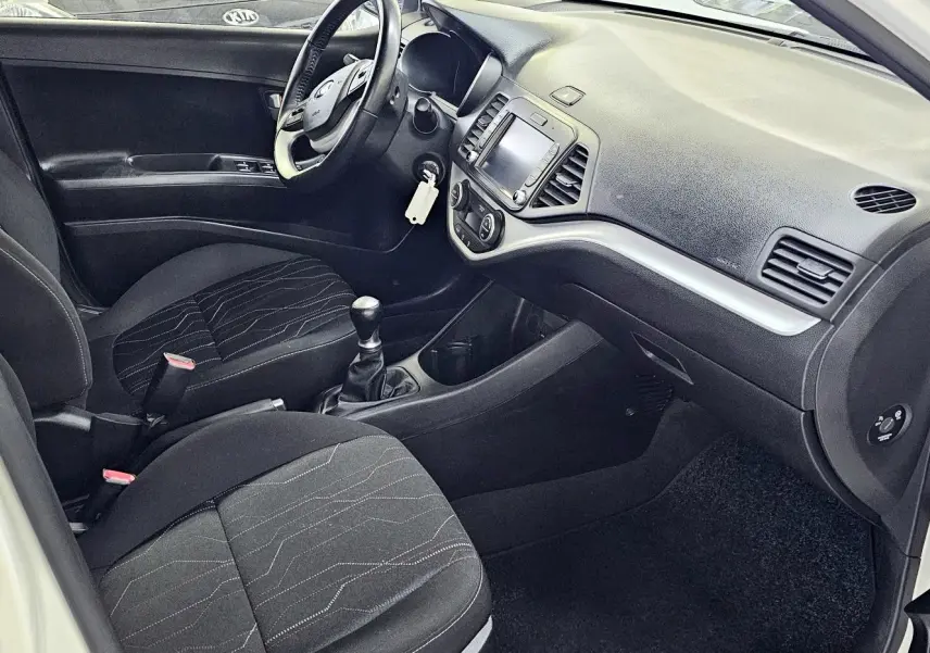 Intérieur noir de la Kia Picanto II blanche 2016, vue côté conducteur avec tableau de bord et boîte manuelle visibles.