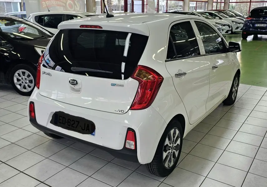 Vue 3/4 arrière droite d'une KIA Picanto blanche 2016 en showroom, avec feux arrière rouges et vitres teintées.