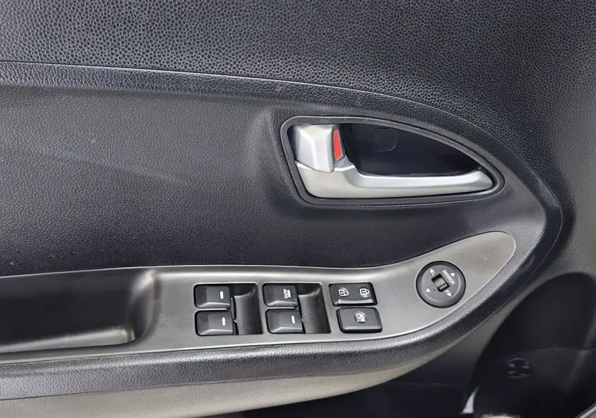 Poignée intérieure côté gauche de la porte d’une Kia Picanto blanche, avec commandes de vitres et rétroviseurs électriques.