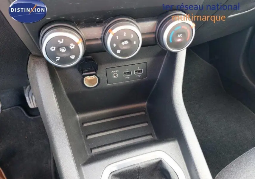 Vue rapprochée de la console centrale noire de la Renault Clio blanche 2021, avec commandes de climatisation manuelle et ports USB.